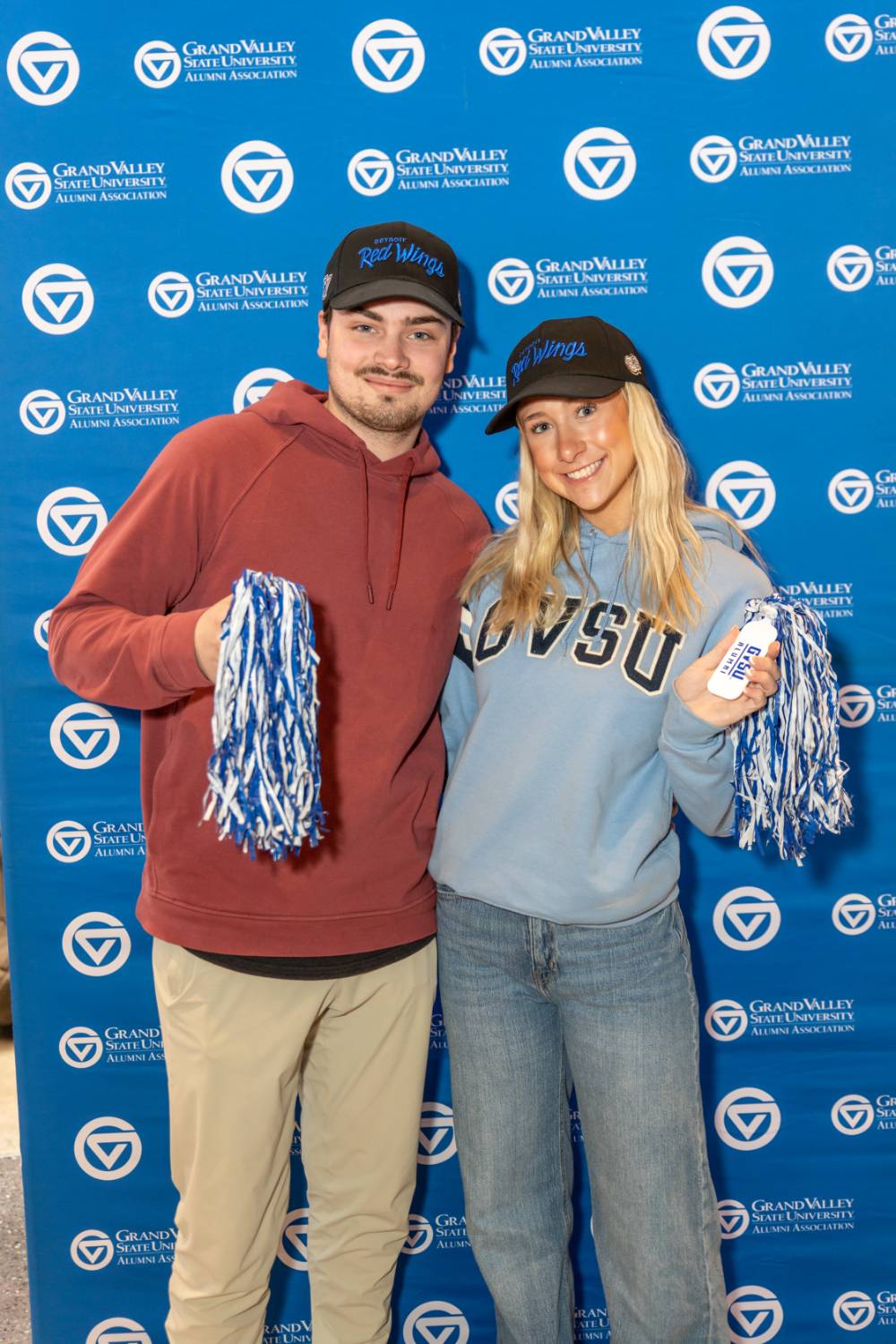 Two alums holding pom poms by the Alumni Relations backdrop